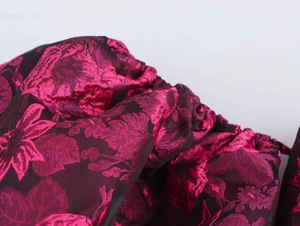 Detailed macro view of dark red jacquard fabric with pink floral texture and shiny finish