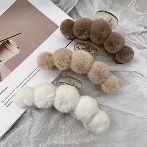 Three large plush hair claw clips in brown, khaki, and white on a soft paper background