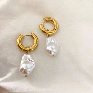 Detailed close-up of golden hoop earrings with baroque pearls on soft white fabric