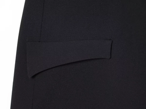 Detailed close-up of a pocket flap on a slim-fit black dress with textured woven fabric