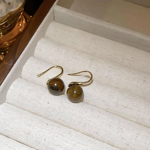 Detail shot of golden metal earrings with polished brown tiger eye beads on a tray