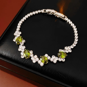 Detail of silver zircon bracelet with green gemstones on black textured background