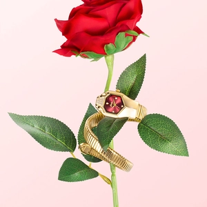 Close-up of golden snake-shaped luxury watch with red dial wrapped around a red rose