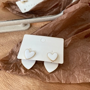 Detail of white heart-shaped earrings with gold edges on jewelry display card
