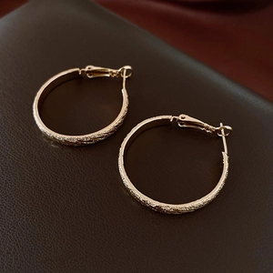 Gros plan de boucles d'oreilles créoles dorées texturées avec finition mate étincelante