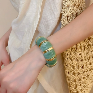 Detailed close-up of emerald green marbled acrylic and gold segment bangle on wrist