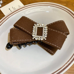 Detail of a dark brown velvet bow hair clip with a sparkling rhinestone buckle on a ceramic plate