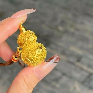 Detail of 24k gold plated hulu pendant with fine carvings and red braided cord