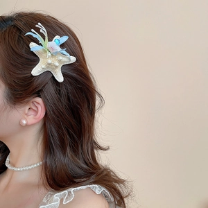 Close-up of starfish hair clip with blue petals and pearls worn by a model