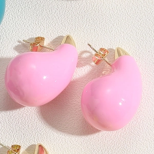 Macro shot of glossy pink teardrop enamel earrings with polished gold metal backings