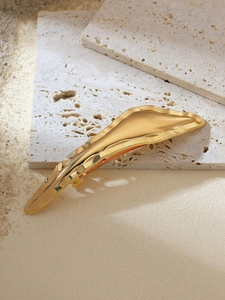 Detailed view of the gold irregular metallic hair clip on a marble and sand background