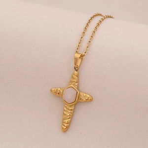 Macro detail of gold cross pendant with hammered texture and hexagonal pink stone