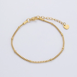 Macro detail of golden box chain bracelet with small beads and heart-shaped S.steel tag