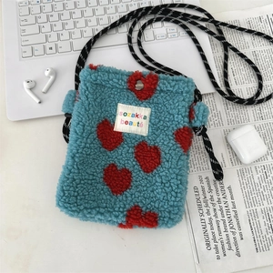 Detail of blue plush crossbody bag with red heart patterns and woven strap