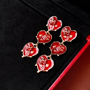 Close-up of triple heart drop earrings with red enamel and gold rose relief on black velvet
