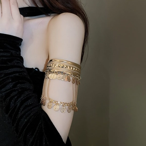 Close-up of golden upper arm cuff featuring bohemian tassels and coin charms detail