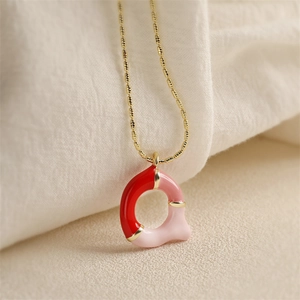 Gros plan du pendentif lettre A doré avec émail rouge et rose sur tissu beige