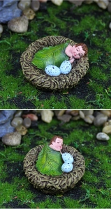 Close-up of a resin fairy garden baby sleeping in a bird nest with green leaf and eggs