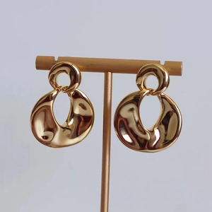 Detail view of 18K gold plated earrings with abstract organic fluid shape on a gold stand