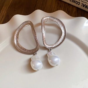 Detailed view of silver leaf earrings with baroque pearl on a white ceramic tray