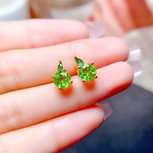 Close-up of gold stud earrings with round green gemstones and leaf-shaped top decorations