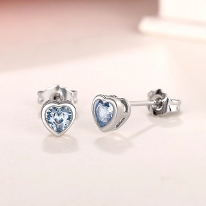 Macro detail of silver heart stud earring with clear light blue heart-shaped gemstone