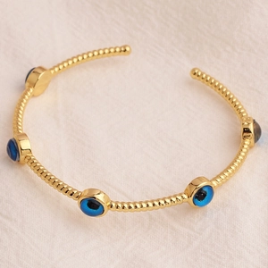 Detail shot of gold-plated twisted rope bracelet with blue evil eye charms on fabric