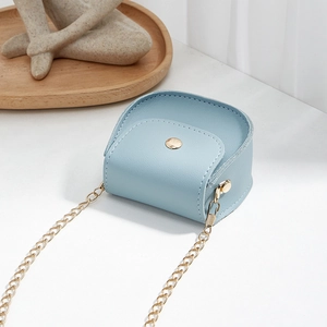 Mini light blue crossbody bag with gold chain and button on a modern artistic background