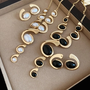 Close-up of gold oval jewelry set with white and black tassels in a beige gift box