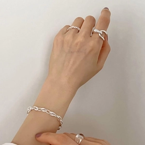 Detailed view of twisted silver rings and chain bracelet on hand with soft lighting