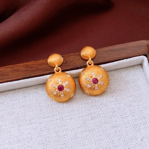 Macro shot of 24k gold-plated earrings featuring a red gemstone and sunburst texture