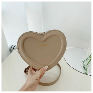 Dettaglio di una borsa a tracolla beige a forma di cuore con scritta dorata Fashion & Bag