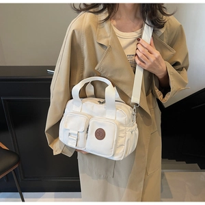 Detailansicht einer weißen Nylon-Umhängetasche mit verstellbarem Riemen auf einem Trenchcoat