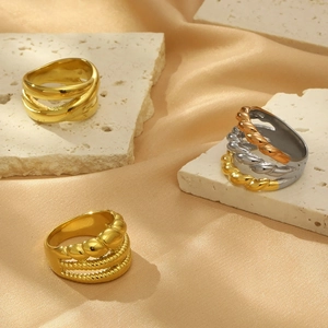 Dettaglio di tre anelli spessi in oro e argento su elegante raso color champagne