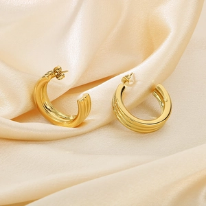 Macro detail of triple-ribbed gold C-shape hoop earrings on premium champagne silk