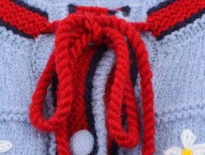 Detail of light blue knit cardigan with red lace-up bow and white floral embroidery