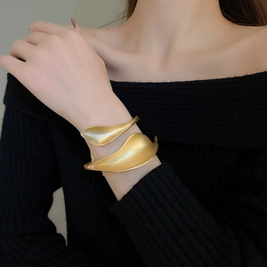 Macro detail of matte gold open bracelet featuring artistic layered leaf design for women