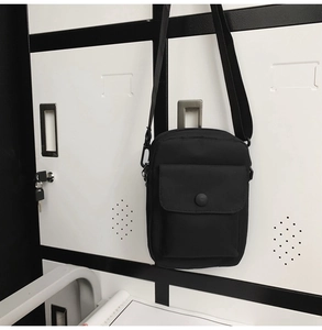 Detail view of black canvas crossbody phone bag featuring adjustable strap and snap pocket