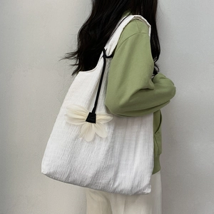 Detail of white pleated canvas tote bag with a large floral charm on a shoulder strap