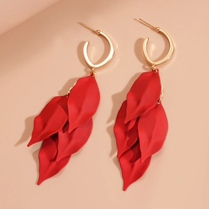 Détail de boucles d'oreilles pétales rouges avec crochets dorés sur fond beige uni