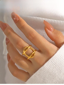 Gros plan d'une bague géométrique ajourée dorée portée par une main de femme