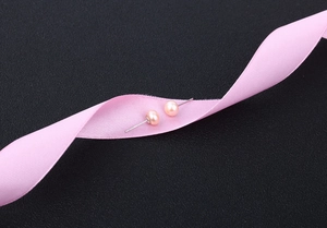 Detailed macro shot of pink freshwater pearl earrings on a silk ribbon over black background