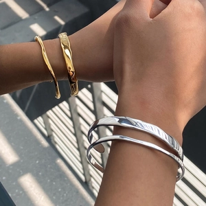 Close-up of layered gold and silver stainless steel wavy bracelets on models' wrists