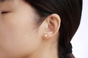 Macro shot of a mini white pearl earring with a gold four-claw base on a model earlobe
