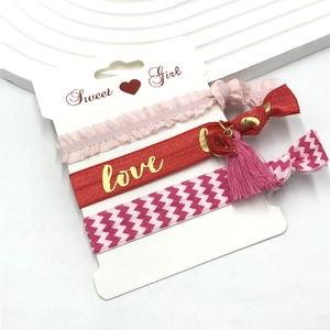 Detailed set of three handmade elastic hair ties with ruffles and love charms on a display card