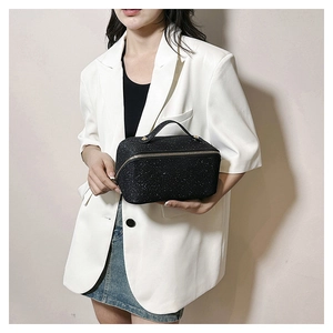 Detail of black glitter makeup bag with gold hardware held by a model in a white blazer