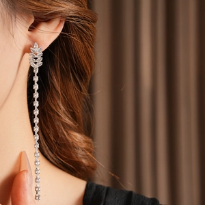 Macro detail of elegant silver tassel earrings with zircon leaf studs on a female model