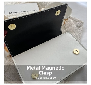 Detail of light gold magnetic clasp and contrast stitching on a two-tone leather handbag