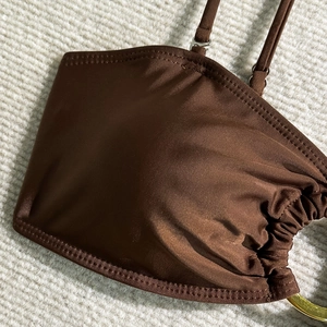 Détail du haut de bikini en satin chocolat avec anneau doré et fronces sur le côté