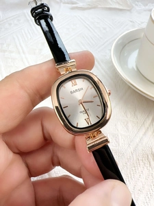 Macro shot of rose gold oval watch with white dial and black leather strap on white fabric